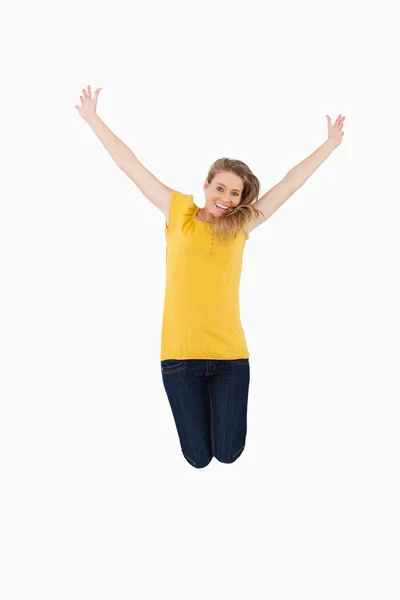 Молодая женщина в жёлтой рубашке прыгает, поднимая руки — стоковое фото