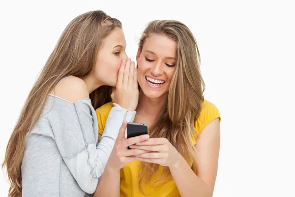 Mujer joven susurrando a su amigo que está enviando mensajes de texto en su teléfono —  Fotos de Stock