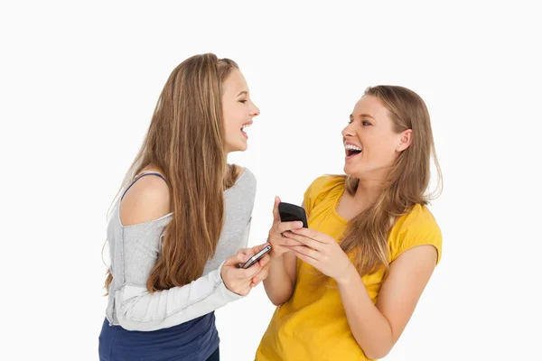 Dos mujeres jóvenes riendo mientras sostienen sus teléfonos celulares —  Fotos de Stock
