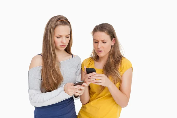 Deux jeunes femmes fronçant les sourcils en regardant leurs téléphones cellulaires — Photo