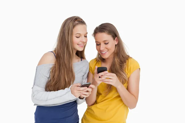 两个年轻妇女微笑时看着他们的手机 — 图库照片