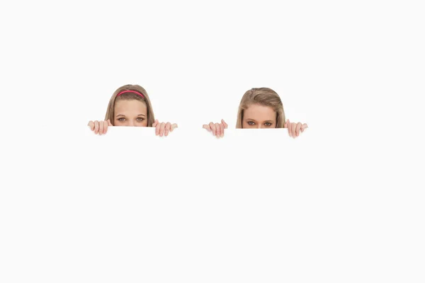 Close-up of young women hiding behind a blank sign — Stock Photo, Image