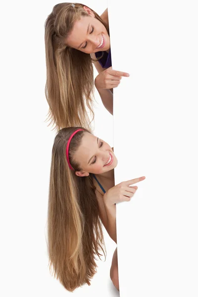 Dois estudantes de cabelos longos apontando atrás de um sinal em branco — Fotografia de Stock