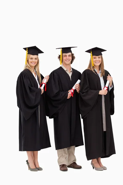 Three smiling students in graduate robe holding a diploma — Stock Photo, Image