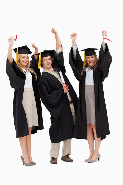 Três estudantes em roupão de pós-graduação levantando os braços — Fotografia de Stock