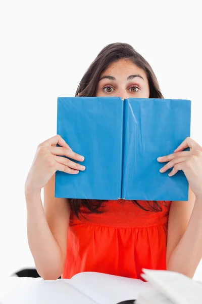 Portrait of a student hiding behind a blue book — Stock Photo, Image