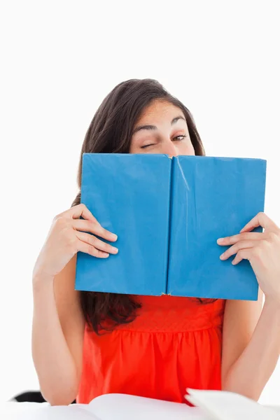 Porträtt av en student som blinka bakom en blå bok — Stockfoto