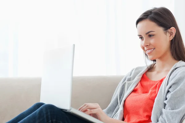 Жінка лежить на дивані посміхається зі своїм ноутбуком — стокове фото