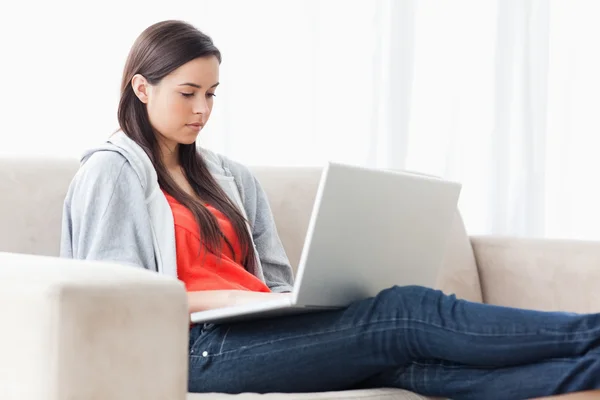 Eine Frau mit ihrem Laptop auf der Couch mit ausgestreckten Beinen — Stockfoto
