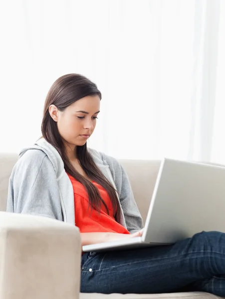 Mulher usando seu laptop como ela se senta no sofá — Fotografia de Stock