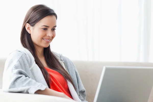 A smiling woman using her laptop as she relaxes on the couch — Stock Photo, Image