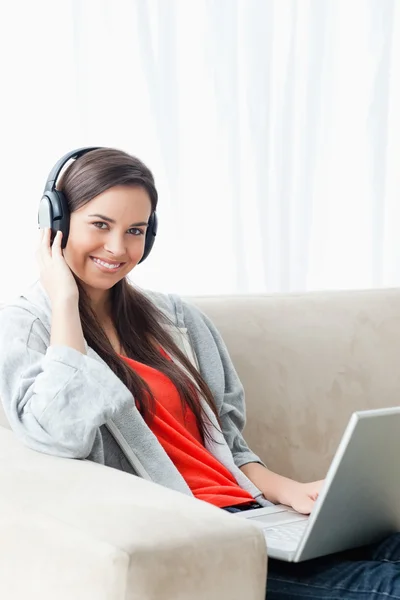 Una joven sonriente usando un portátil y auriculares mientras mira —  Fotos de Stock