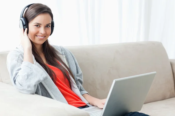Usmívající se žena drží sluchátka a přenosný počítač při pohledu na — Stock fotografie