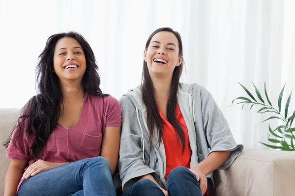 Две женщины сидят рядом на диване и смеются. — стоковое фото