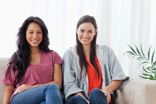 Två leende kvinnor sitter på soffan tillsammans medan du tittar på den — Stockfoto