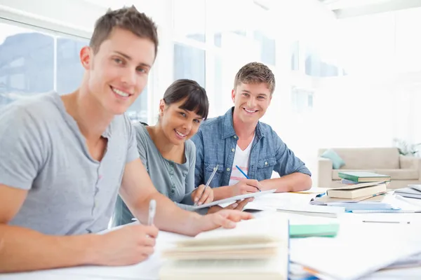 Трое улыбающихся студентов делают домашнее задание, глядя в пришли — стоковое фото