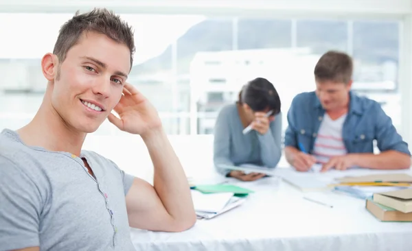 A smirking student sits in front of his friends as he looks into — Stock Photo, Image