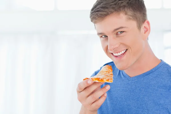 Un uomo con un pezzo di pizza mentre guarda la telecamera — Foto Stock