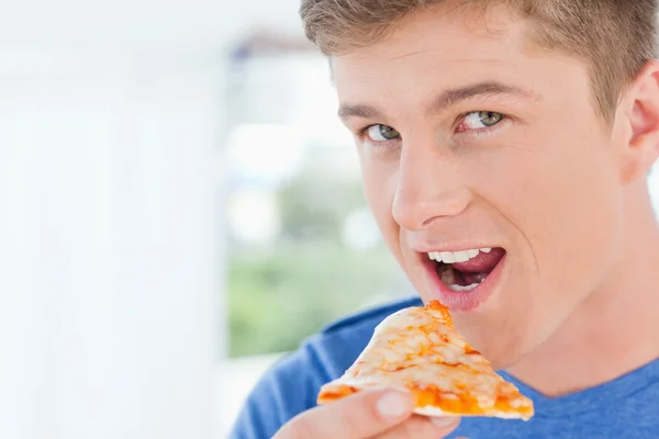 Ein Mann mit einem Stück Pizza in der Hand, während er den Kameramann ansieht — Stockfoto