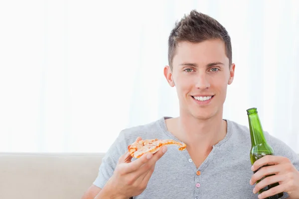 Мужчина улыбается с пивом в одной руке и пиццей в другой — стоковое фото
