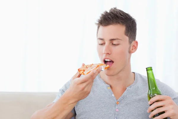 Um homem prestes a comer pizza enquanto segura uma cerveja — Fotografia de Stock