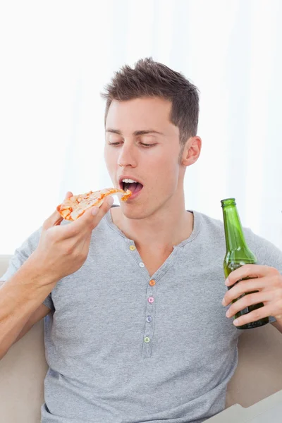 Een man met een stuk van pizza en bier in zijn handen — Stockfoto