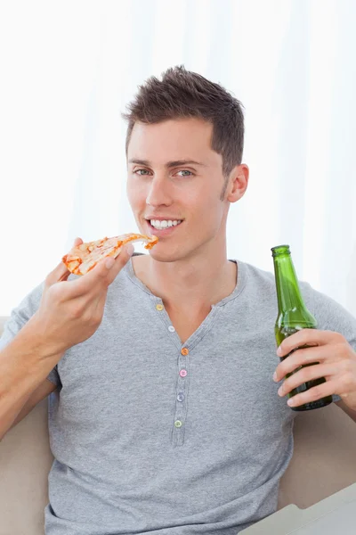 Un hombre sonriente sentado con pizza en una mano y cerveza en la otra —  Fotos de Stock