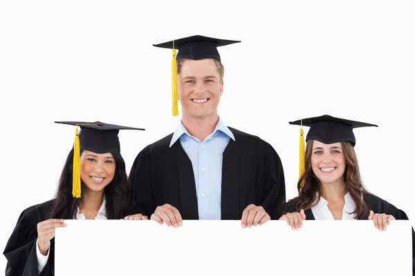 Three students having graduated holding a blank poster — Stock Photo, Image
