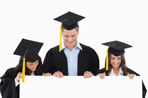 Três estudantes tendo se formado segurando folha em branco e olhando — Fotografia de Stock