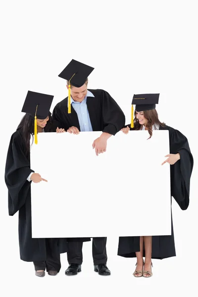 Три випускники, які вказують на порожній знак — стокове фото