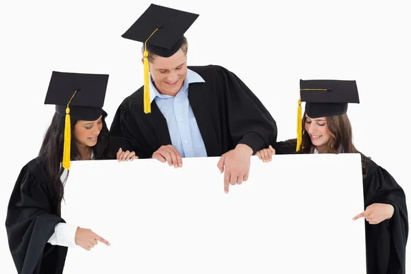 Três graduados apontando para o sinal em branco — Fotografia de Stock