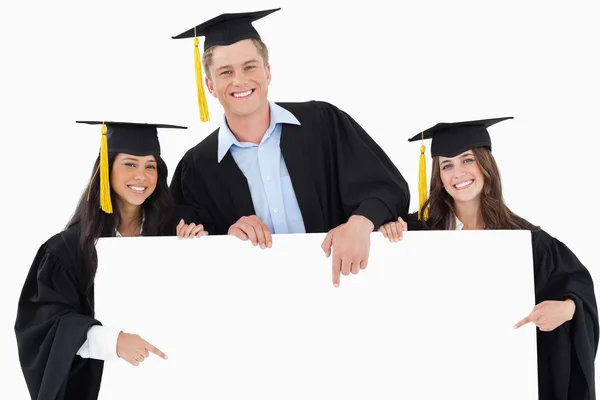 Three graduates pointing to the blank sign as they look at the c — Stock Photo, Image