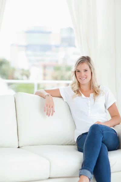 Eine Frau mit dem Arm auf der Couch sitzend und lächelnd — Stockfoto