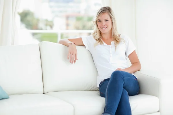 Una mujer sonriendo mientras se relaja en el sofá con las piernas cruzadas — Foto de Stock
