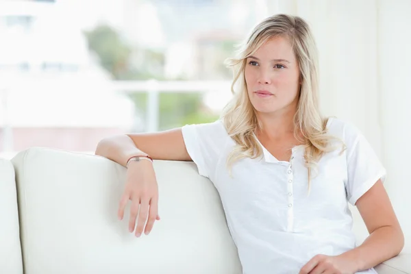 A woman looking to the side as she sits on the couch — Stock Photo, Image