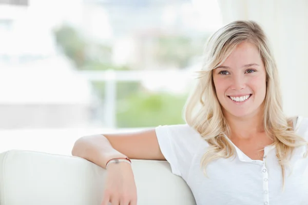 Uma mulher sorrindo enquanto se senta no sofá e olha para o lado — Fotografia de Stock