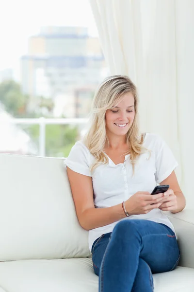 Une femme sourit en utilisant son téléphone sur le canapé — Photo