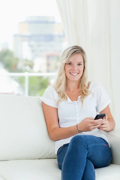 Eine lächelnde Frau hält ihr Handy in der Hand, während sie sitzt und auf das c schaut — Stockfoto