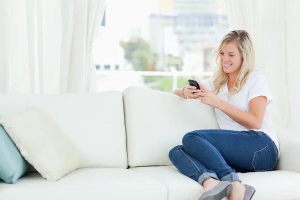 Žena sedí na gauči na stranu, jak ona používá její telefon — Stock fotografie