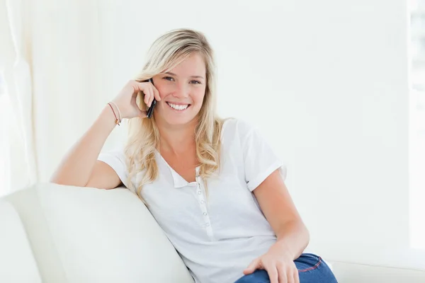 Вид сбоку на женщину на диване, улыбающуюся, когда она разговаривает по телефону — стоковое фото