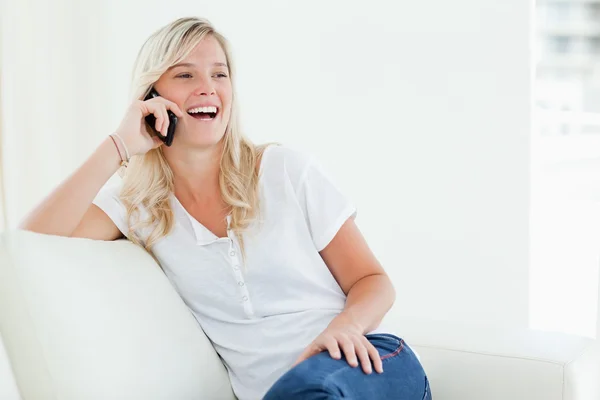 En skrattande kvinna på sin telefon som hon sitter på soffan — Stockfoto
