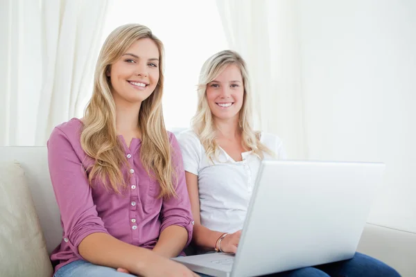 Sisters sitting on the couch looking at the camera as they hold — Stock Photo, Image