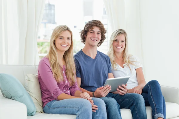 Drei junge Erwachsene blicken in die Kamera, während sie ein Tablet in der Hand halten. — Stockfoto