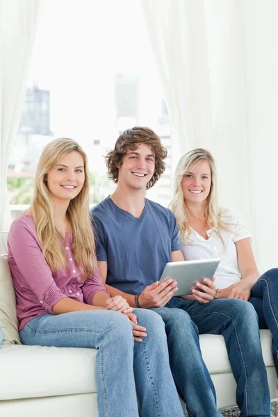 Two sisters and a brother sit on the couch looking at the camera — Stock Photo, Image
