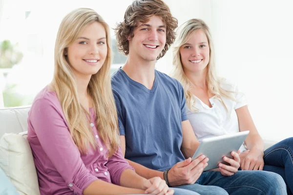 Three siblings sit together as they use a tablet and look at the — Stock Photo, Image