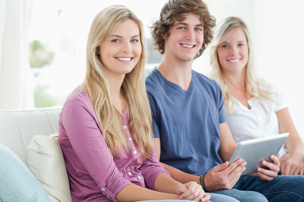 Tres sonrientes se sientan juntos en el sofá con una tableta —  Fotos de Stock