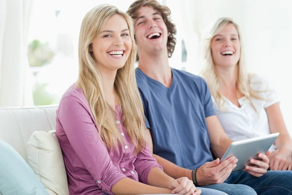 Lachende Gruppe von Freunden sitzt, während sie ein Tablet benutzen — Stockfoto