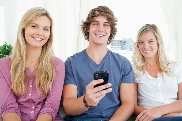 Drei Freunde blicken in die Kamera, als der Junge ein Handy in der Hand hält. — Stockfoto