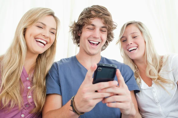 Três amigos olhando para a tela de um telefone celular enquanto smil — Fotografia de Stock
