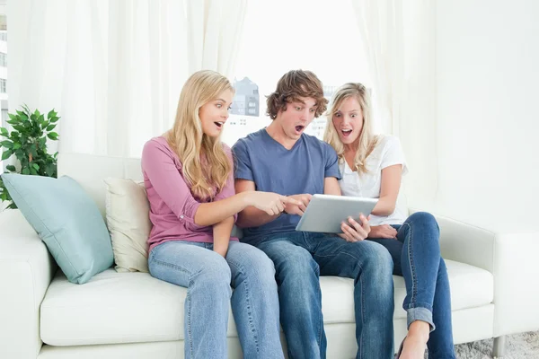 Drei Freunde blicken schockiert auf den Bildschirm des Tablets und — Stockfoto